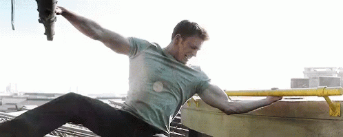 Captain America flexing his bicep as he grabs on to the skid of a helicopter and the edge of a helipad to prevent the helicopter from flying away.