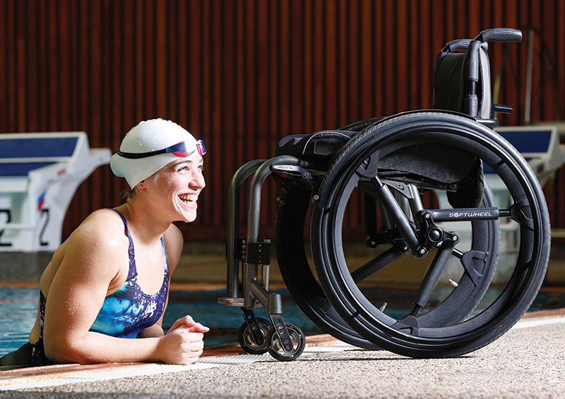 An image of a woman half-way out of a swimming pool. Her wheelchair is in\nfront of her. It uses a pair of NuMotion SoftWheels.
